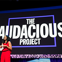 A woman in front of a large media screen projection