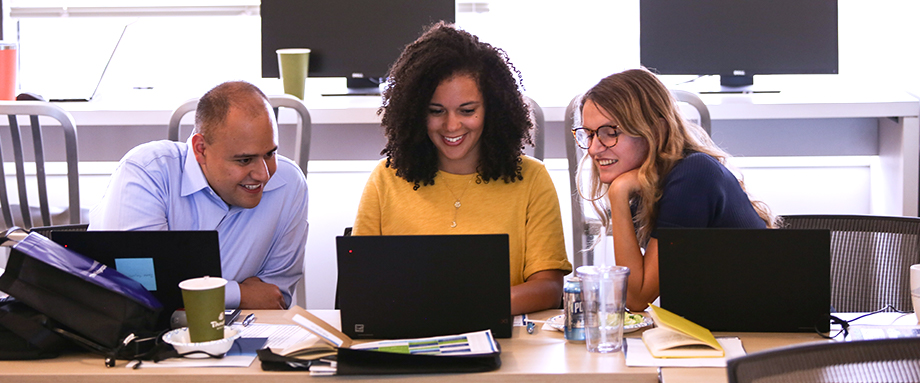 Three team members collaborating around a laptop