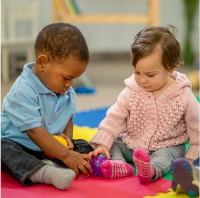 Two infants playing on a mat