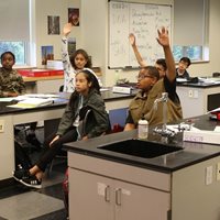 Children in a classroom with hands up