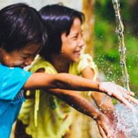 Two smiling children with hands in a stream of water