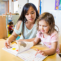 A teacher helping a student reading a book